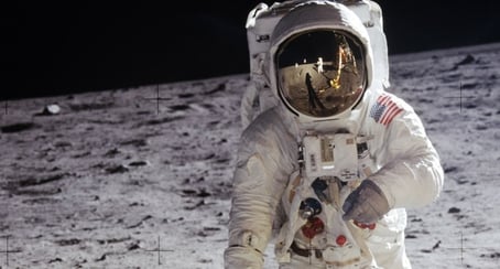 Astronaut (Buzz Aldrin) standing on the moon with reflection of astronaut (Neil Armstrong) and lunar module in his helmet's visor