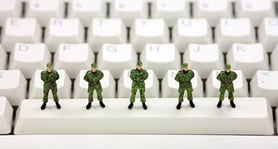 Five tiny toy soldiers lined up on the space bar of a computer keyboard