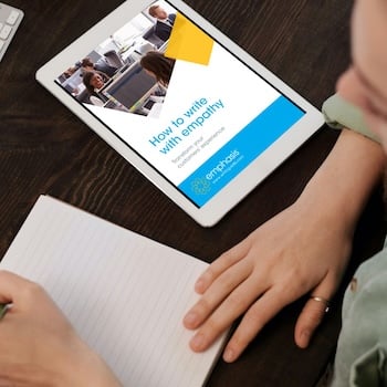Person writing on notebook with tablet displaying How to write with empathy guide next to them